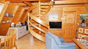 A cozy, wooden interior with a spiral staircase, a dining area, a sofa, and a television.