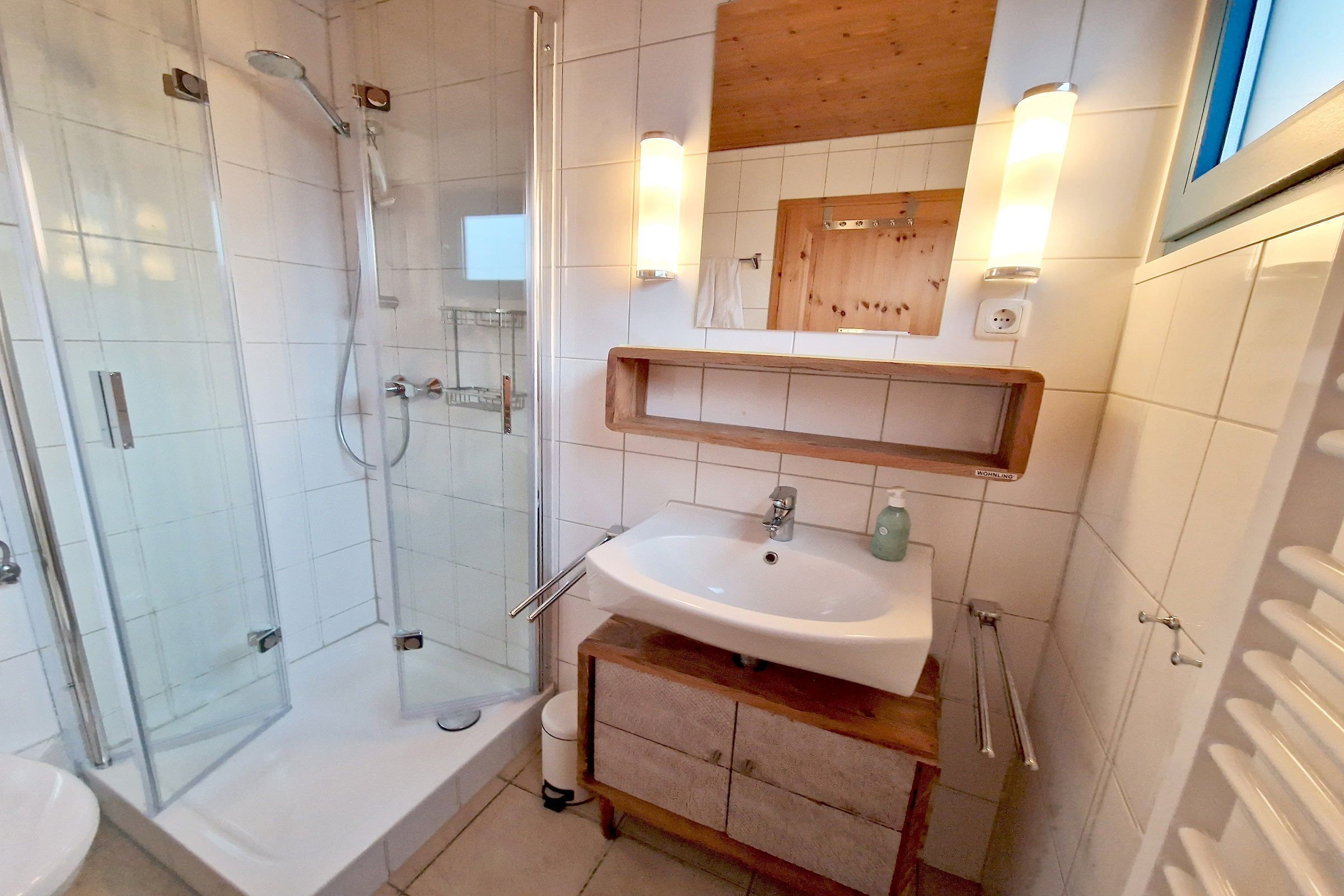 Ein Badezimmer mit einer gläsernen Duschkabine, einem weißen Waschbecken und einem hölzernen Waschtisch.