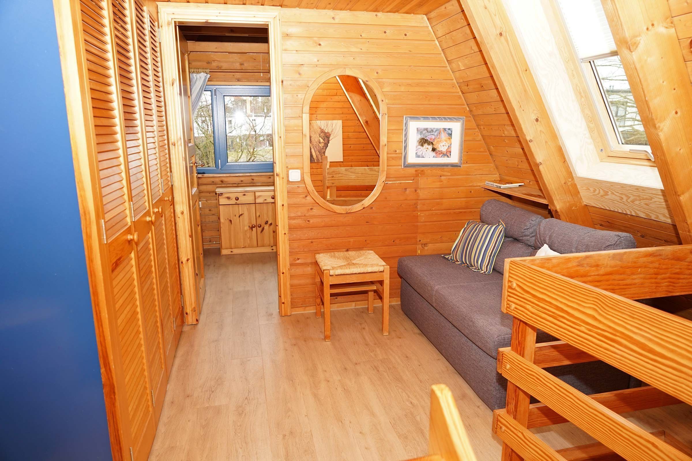 Um quarto de sótão acolhedor, com paredes de madeira, um sofá, uma mesinha e uma janela.