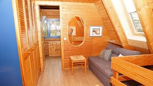 A cozy attic room with wooden walls, a sofa, a small table, and a window.