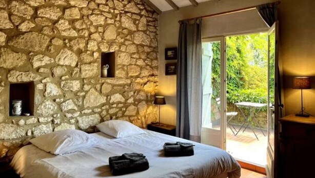 Ein Schlafzimmer mit Steinwand, einem Bett mit weißen Leinen, einem Nachttisch und Blick auf einen Garten durch eine Glastür.