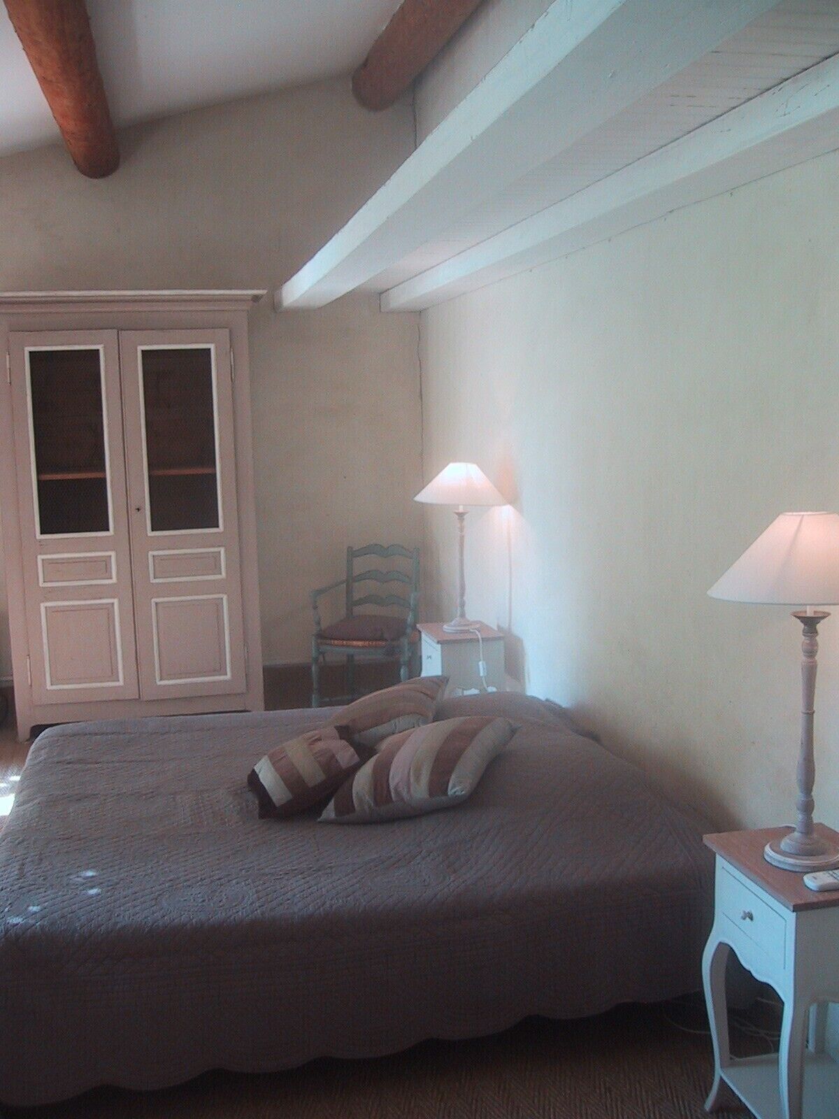A bedroom with a bed, a chair, a nightstand, and a wardrobe.