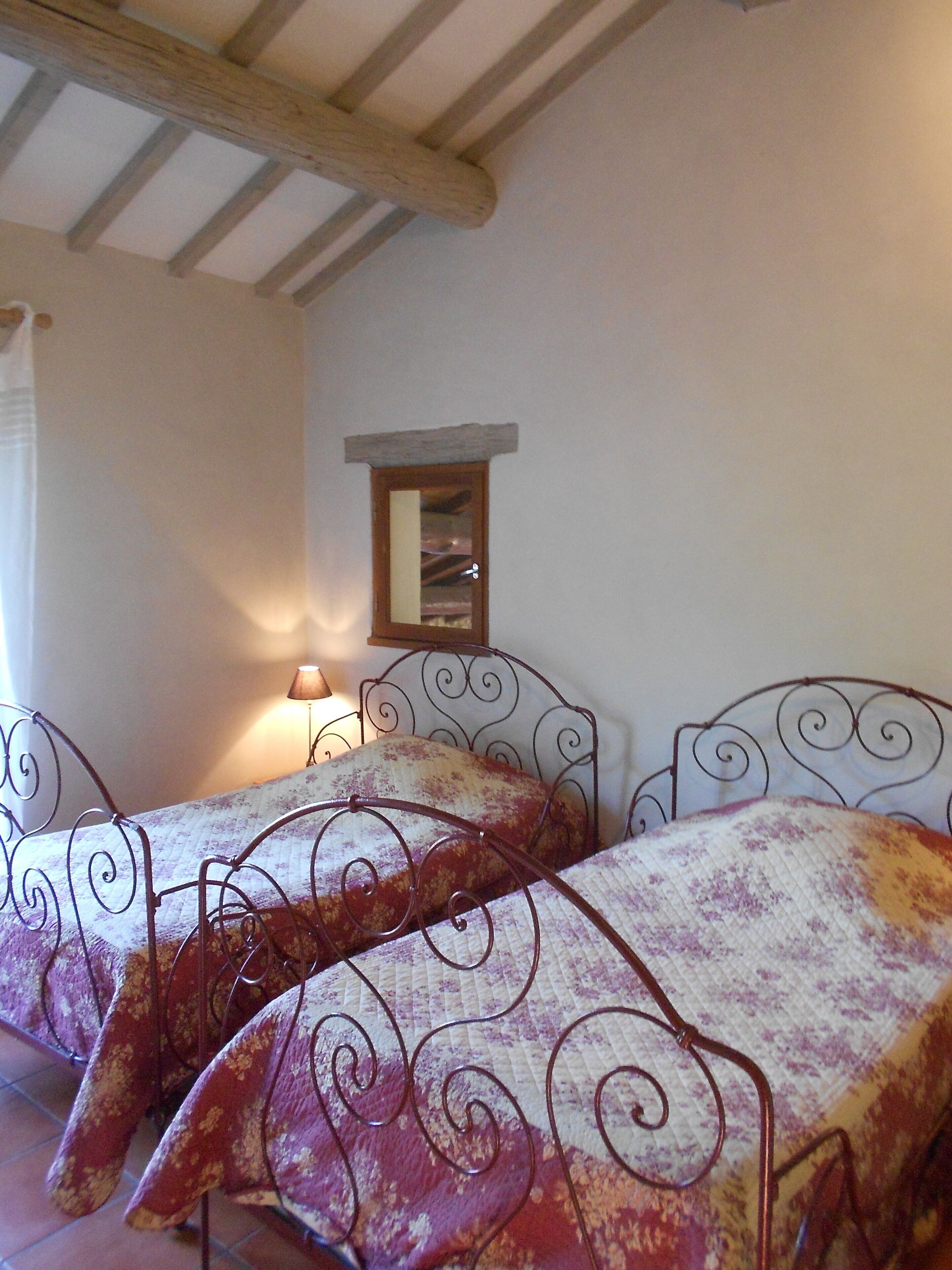 A bedroom with two beds, a wooden ceiling, a small mirror, and a lamp.
