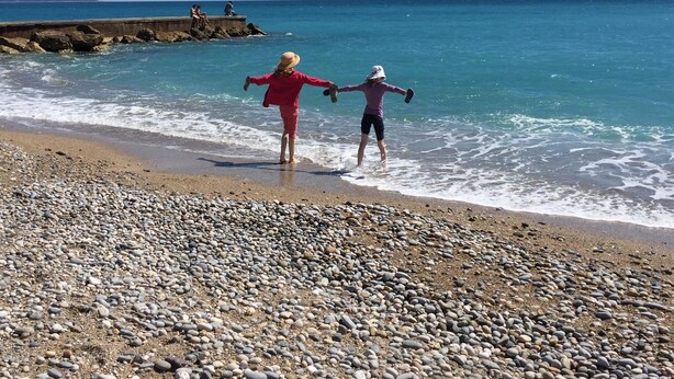 A pebbled beach with two people walking towards the water. - Magnifique appartement dominant de 100m2, énorme terrasse vue mer et montagne (Vence)
