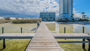 Un molo in legno che conduce a un edificio dal design moderno, affacciato su un'acqua calma e con cieli sereni.