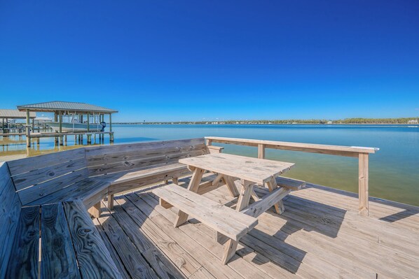 A wooden deck with picnic tables and benches overlooking a calm lake.
