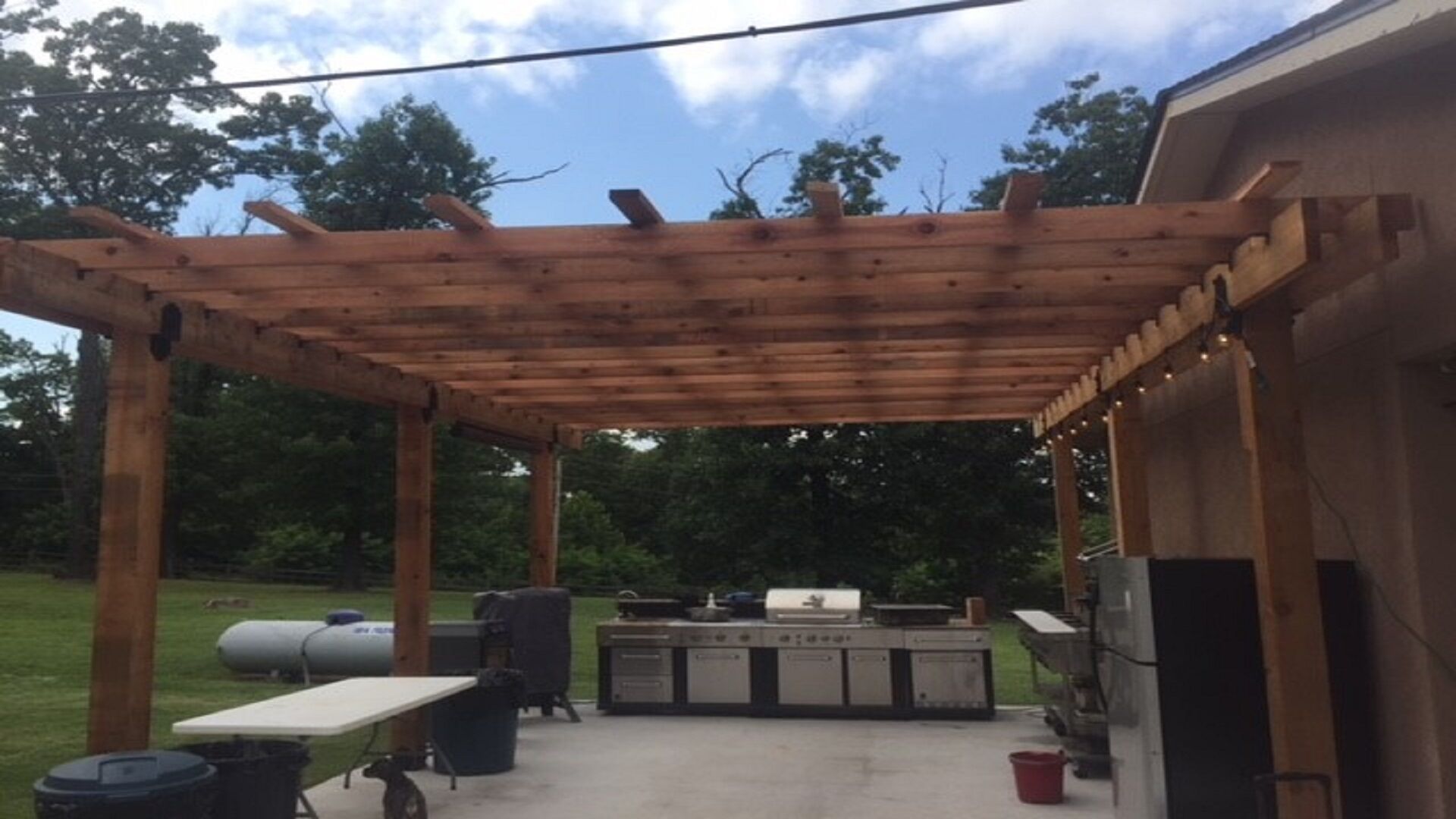 Una pergola in legno con un angolo barbecue sottostante, comprensivo di griglia e lavandino.