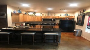 A modern kitchen with wooden cabinets, a black refrigerator, stainless steel appliances, and a bar area with stools. - HEATED POOL  Grand Serenity is your Oasis on South Grand (Afton)