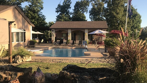 A pool area with lounge chairs, a flag, and a building with a 'Welcome' sign. - HEATED POOL  Grand Serenity is your Oasis on South Grand (Afton)