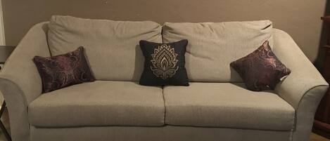 Un sofá beige con tres almohadones decorativos frente a una pared lisa.
