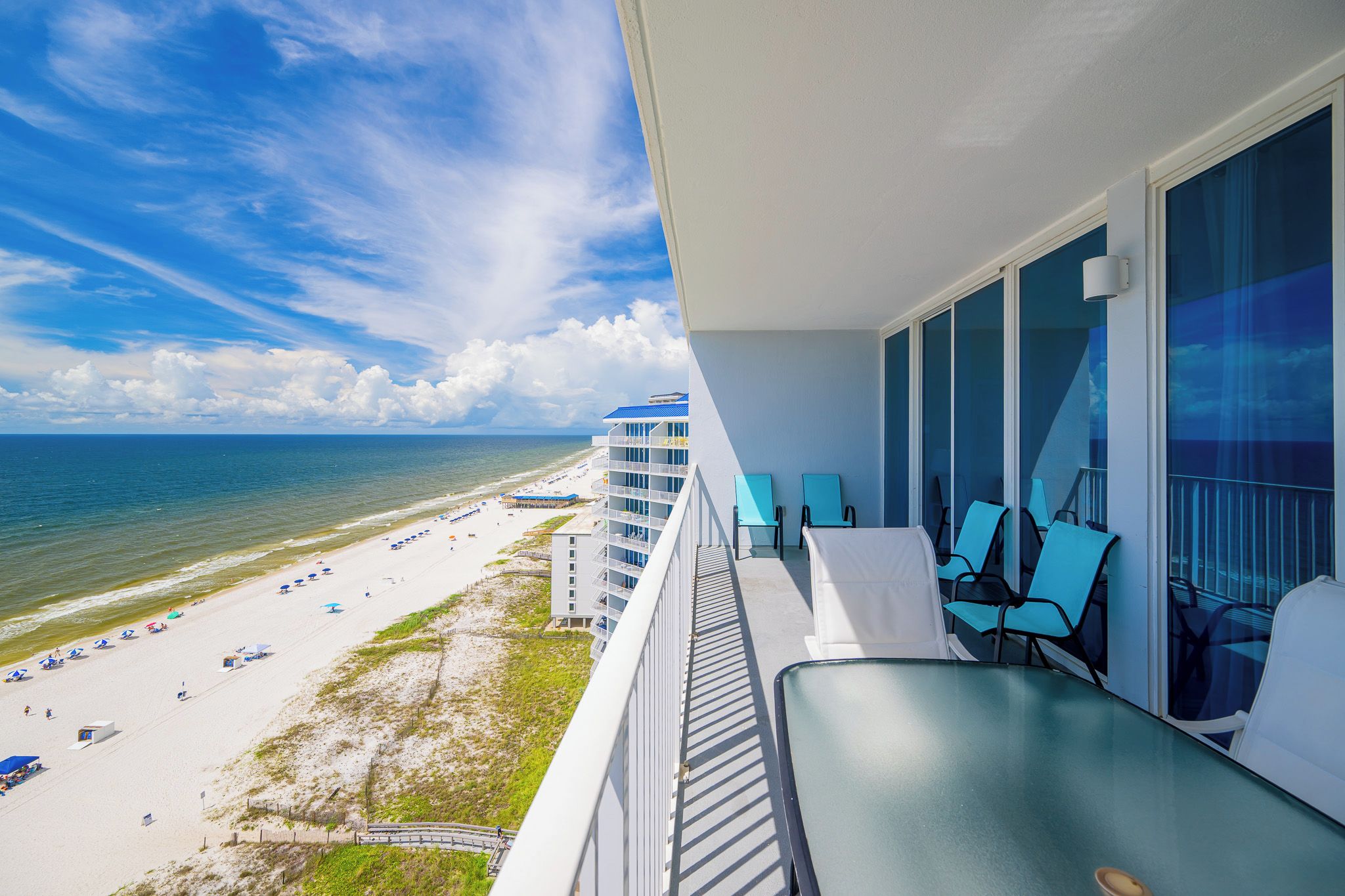 Ein Balkon mit Blick auf Strand und Meer, ausgestattet mit einem Glastisch und Stühlen.