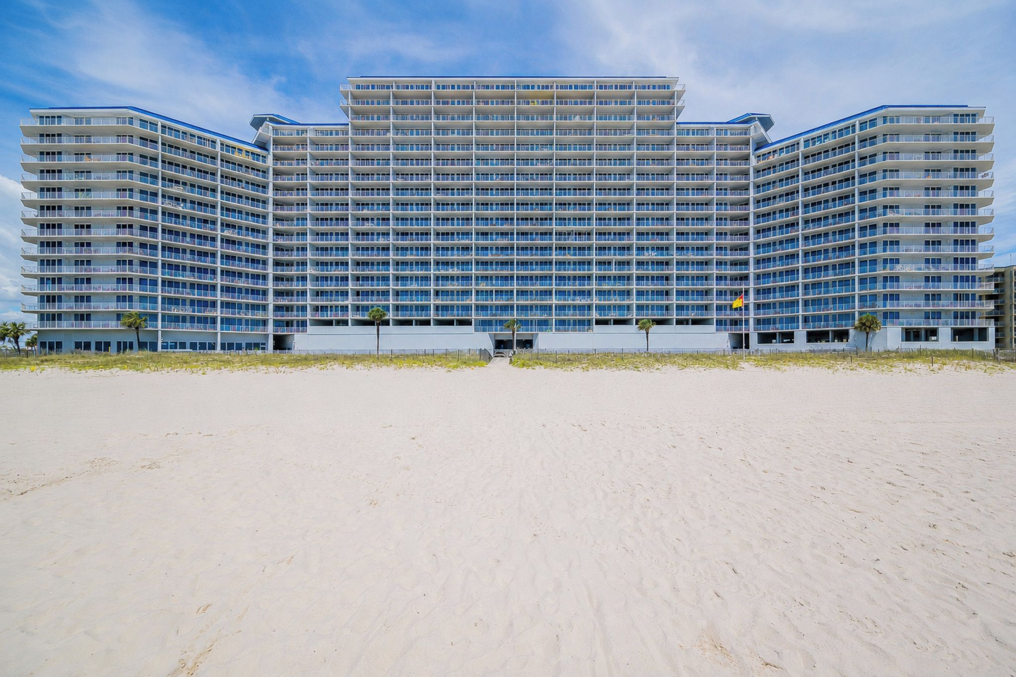 A large hotel with multiple floors and balconies, situated on a sandy beach.