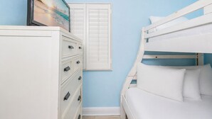 Een slaapkamer met een stapelbed, een dressoir met lades en een raam met luiken.