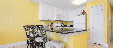 A kitchen with white cabinets, a central island, bar stools, and a microwave.