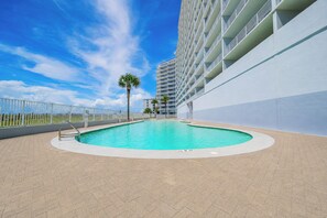 A swimming pool with a white pool deck, surrounded by a white fence, and a tall building in the background. - LIGHTHOUSE! Popular Property! ~ 1 BR Beach Front! XTRA BATH! (Gulf Shores)