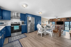 A modern kitchen with blue cabinets, stainless steel appliances, and a dining area with white chairs.