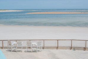 A beach view with a concrete deck and white chairs.