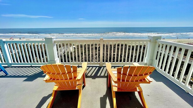 Een balkon met twee houten stoelen gericht op het strand.