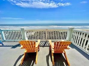A balcony with two wooden chairs facing a beach.