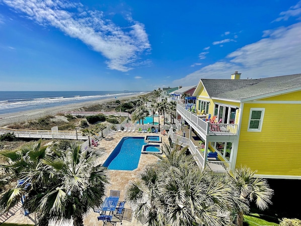 A beachfront property with a swimming pool, multiple balconies, and a view of the ocean.