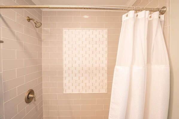 A shower area with beige tiles, a white patterned towel, and a white shower curtain.