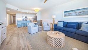 Ein modernes Wohnzimmer mit einem blauen Sofa, einem runden Couchtisch und einer Küche im Hintergrund.