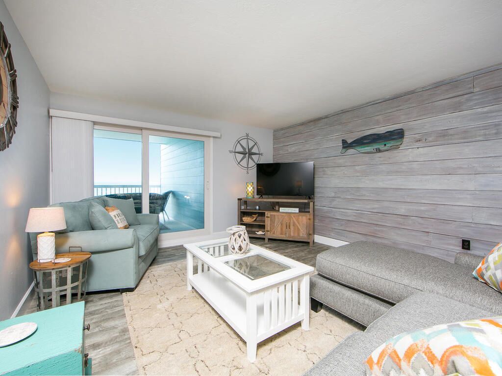 A living room with a sofa, a coffee table, a TV, and a wooden wall with a fish decoration.