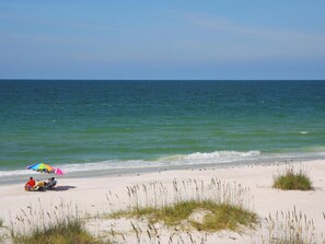 A beach with a clear view of the ocean, a sandy shore, and a few people under umbrellas.