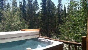 A hot tub with a wooden deck and a view of a forest.