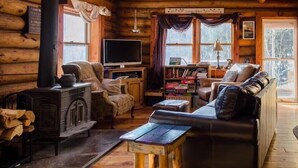 A cozy log cabin interior with a fireplace, a sofa, a television, and a bookshelf.