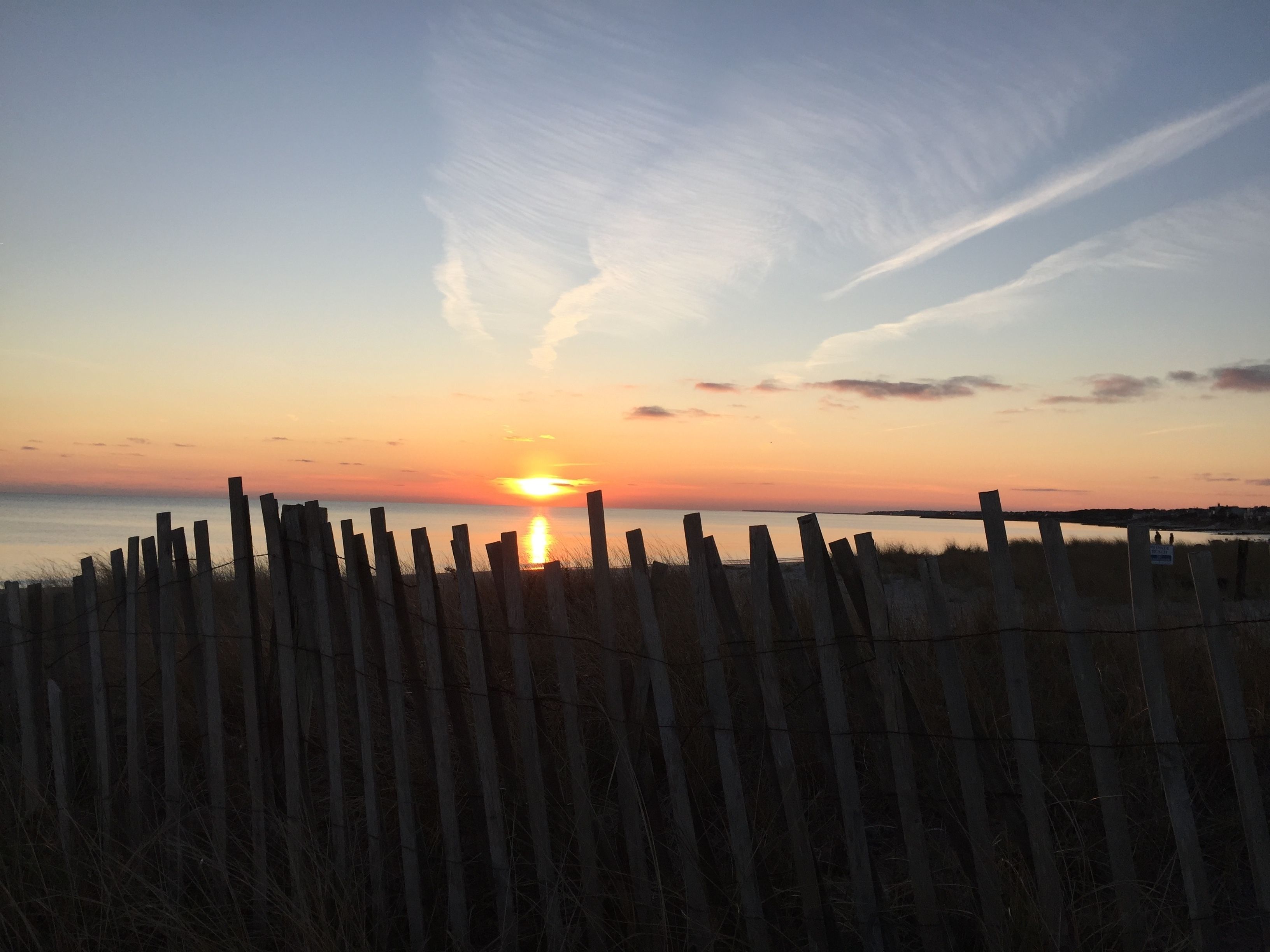 A sunset over a calm body of water, viewed through a wooden fence.