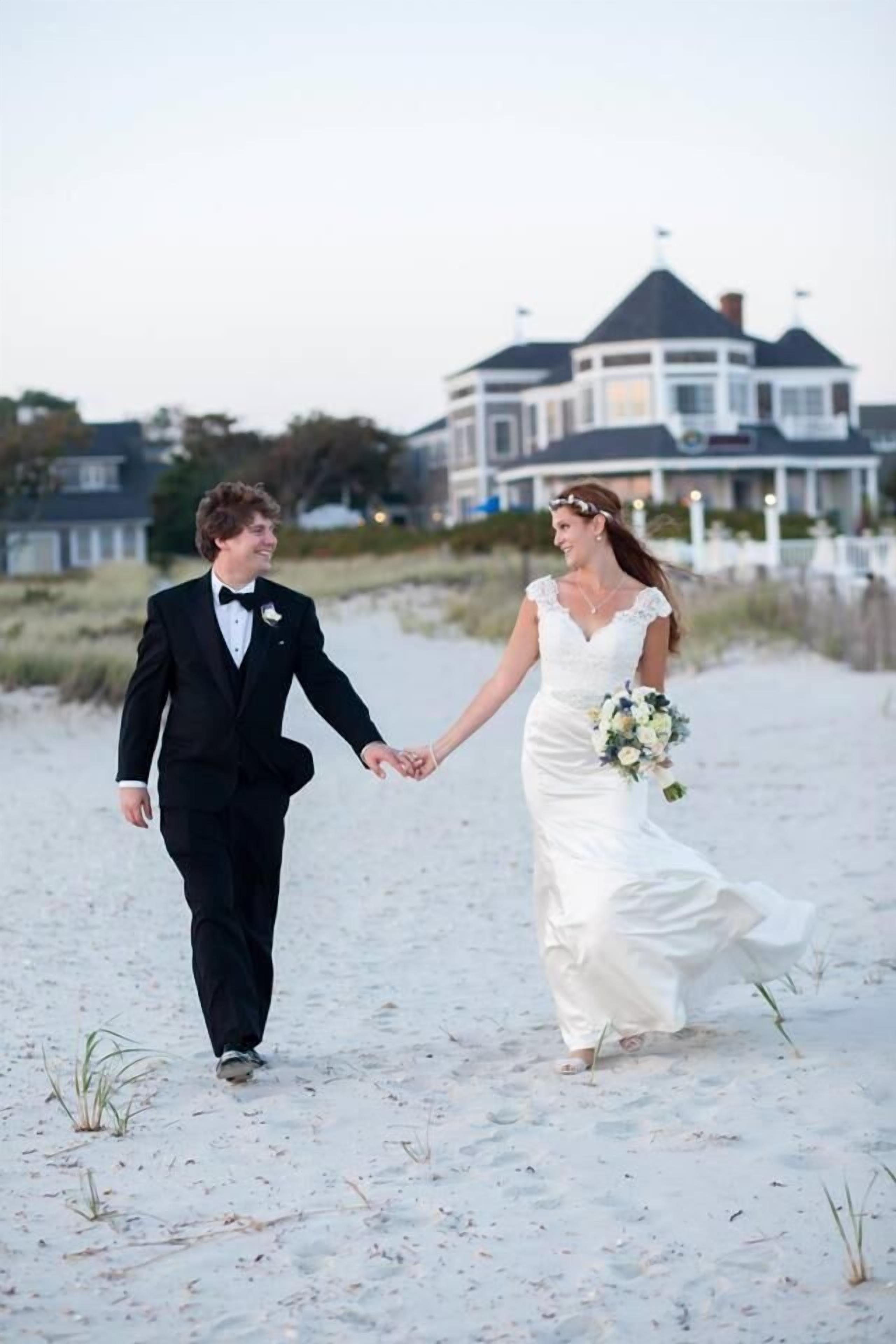 A couple walking on a sandy beach holding hands.