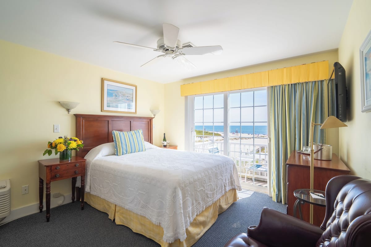Une chambre d’hôtel équipée d’un lit, d’un bureau, d’une chaise, d’un ventilateur de plafond, d’une fenêtre avec des rideaux et offrant une vue sur la plage.
