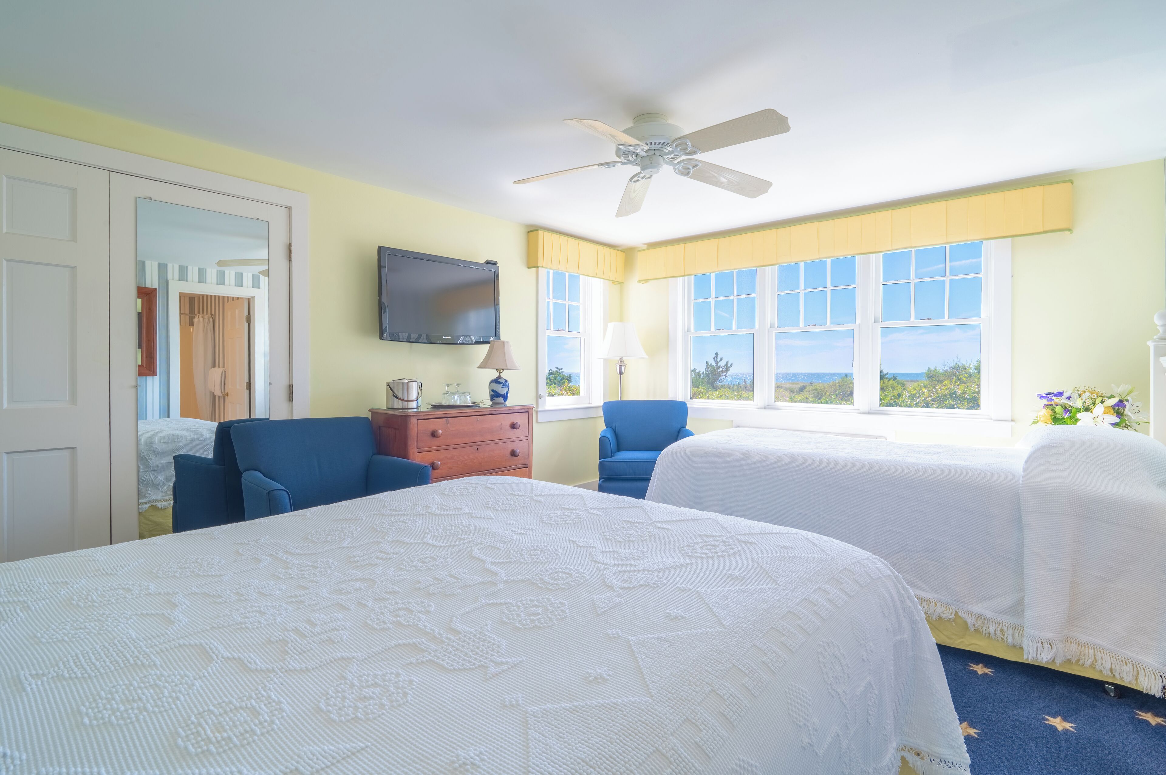 Une chambre d’hôtel avec deux lits, un ventilateur de plafond, une télévision et une fenêtre donnant sur un paysage agréable.