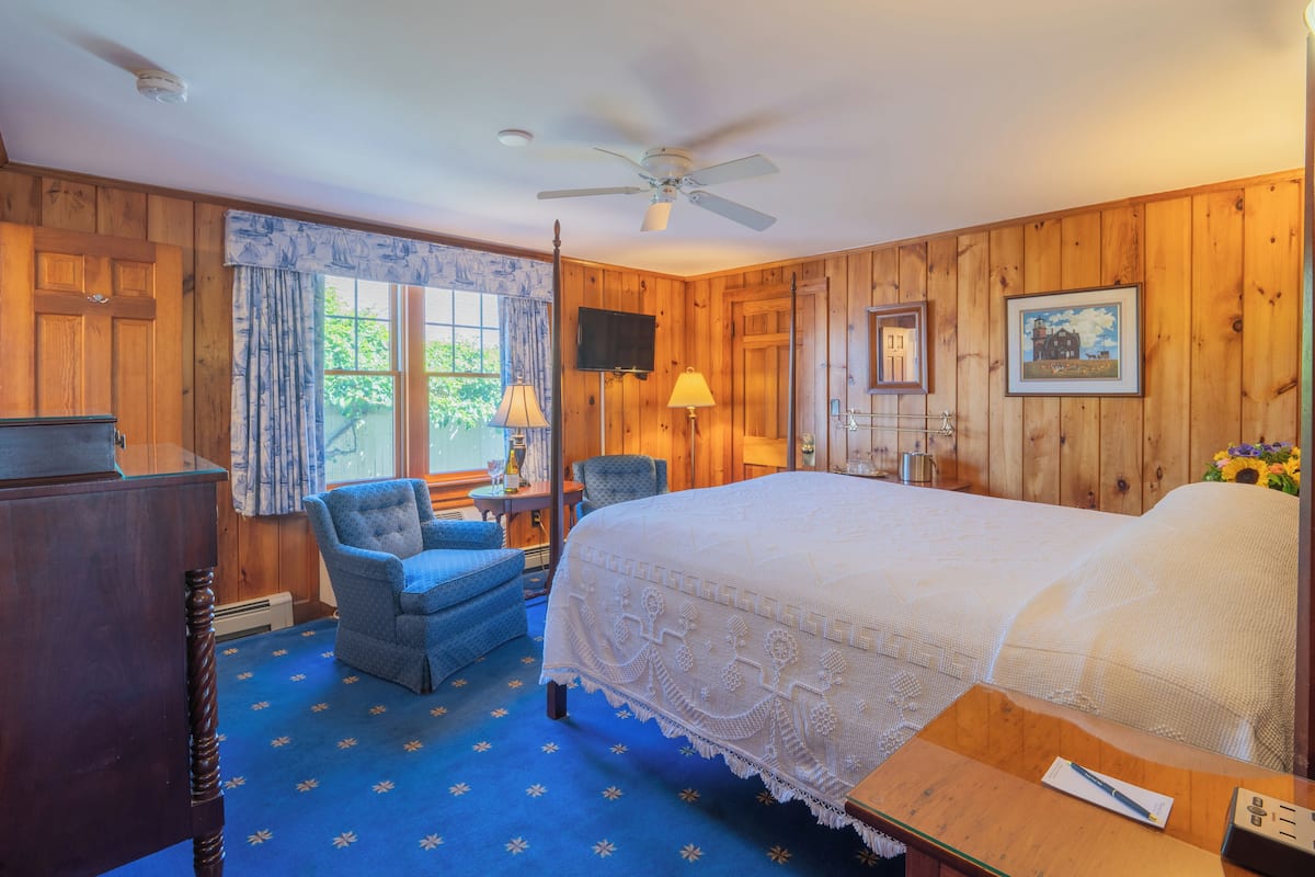 Une chambre avec un grand lit, une chaise, un bureau et un ventilateur de plafond.
