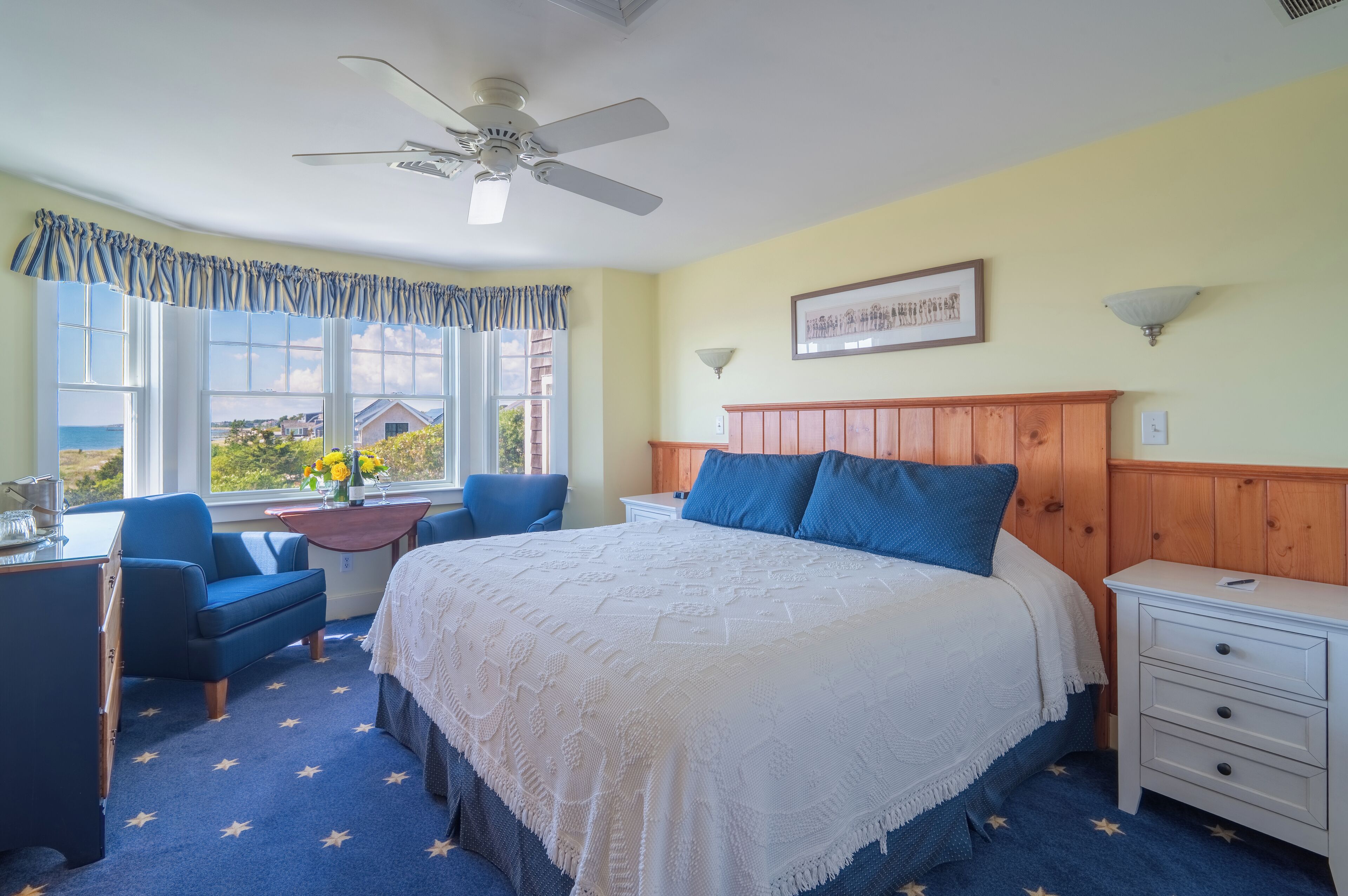 A bedroom with a bed, a desk, a chair, a nightstand, and a window with a view of the outside.