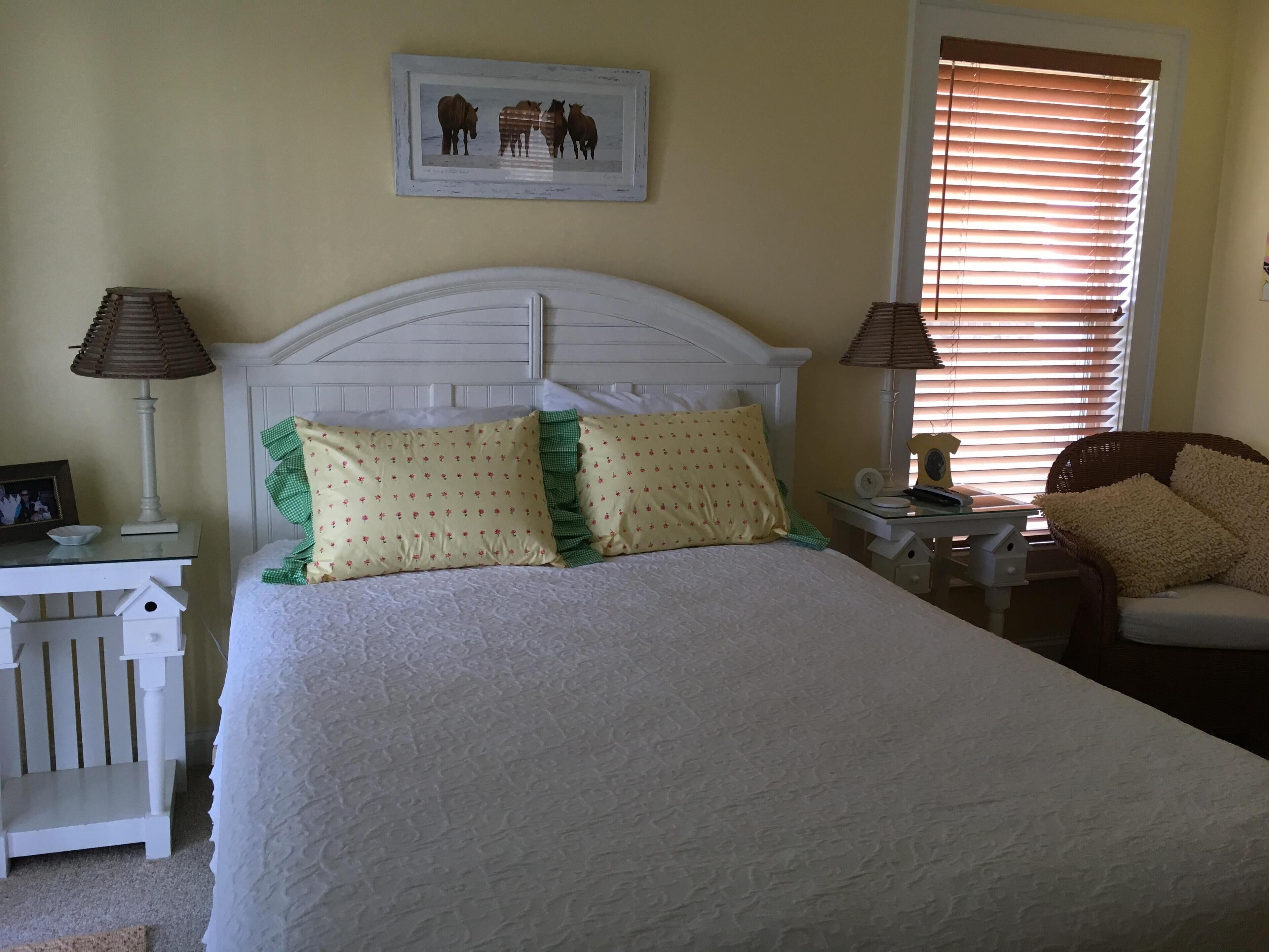 A neatly arranged bedroom with a bed, two bedside tables, a chair, and a window with blinds.