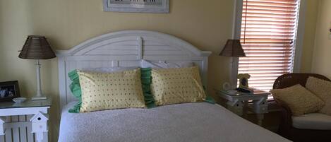A neatly arranged bedroom with a bed, two bedside tables, a chair, and a window with blinds.