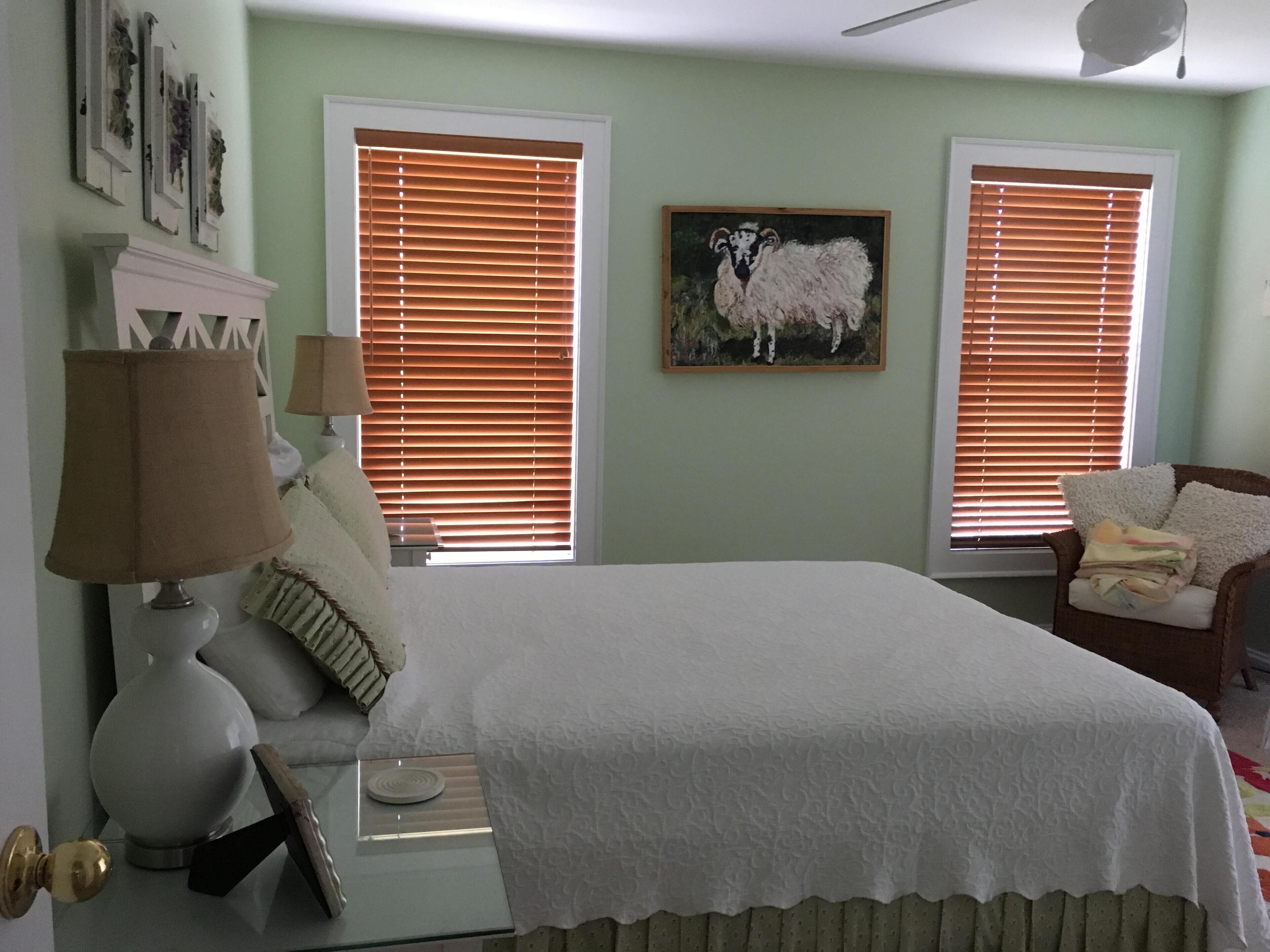 A bedroom with a bed, two windows with blinds, a chair, and a lamp.