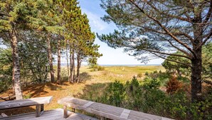 Una terraza de madera con bancos que da a un paisaje natural con árboles y una vista distante del horizonte.