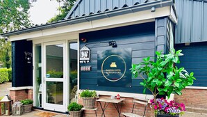 A Gasterij Hotel Dennenoord with a dark exterior, a welcoming entrance, and outdoor seating area with potted plants and a small table. - Gasterij Hotel Dennenoord (Boxtel)