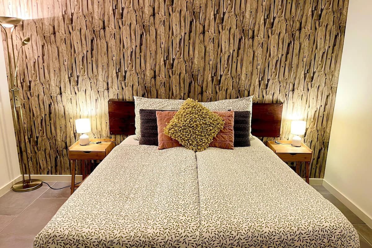 A bed with a patterned bedspread, two bedside tables with lamps, and a wall with a vertical wooden texture.