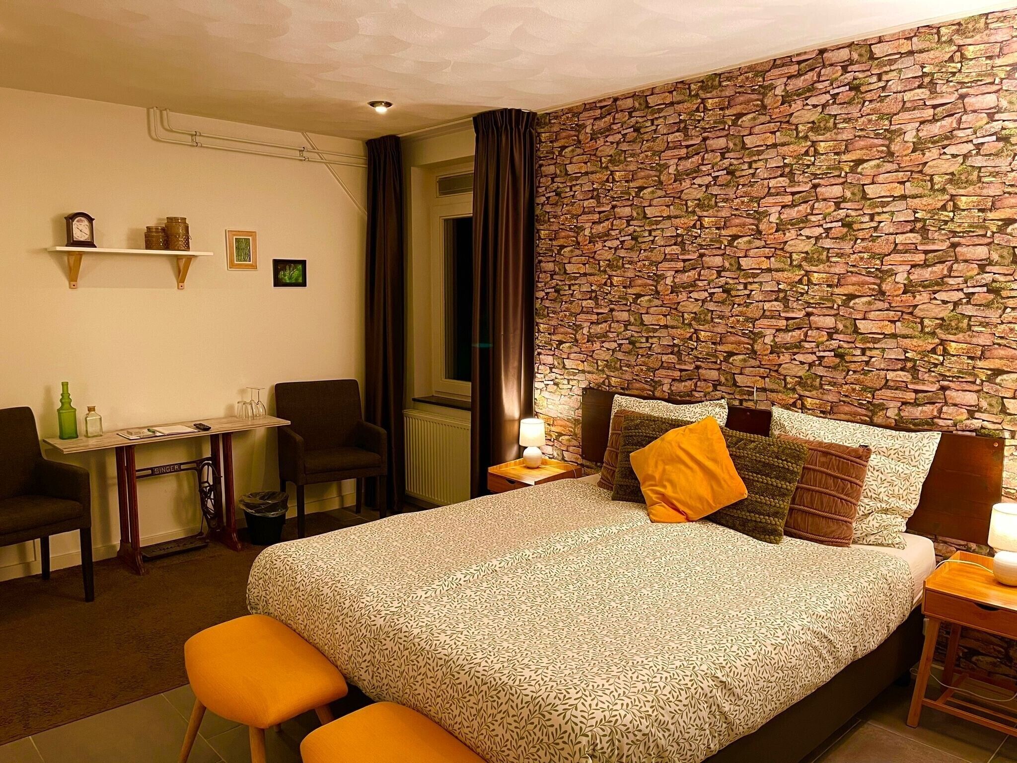 A hotel room with a bed, a desk, a chair, and a stone wall.