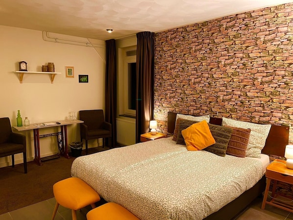 A hotel room with a bed, a desk, a chair, and a stone wall. - Gasterij Hotel Dennenoord (Boxtel)