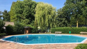 A rectangular swimming pool with a brick deck, surrounded by lush greenery and trees. - Gasterij Hotel Dennenoord (Boxtel)