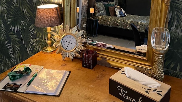 A wooden dresser with a mirror, a clock, a lamp, a tissue box, and a notebook. - Gasterij Hotel Dennenoord (Boxtel)
