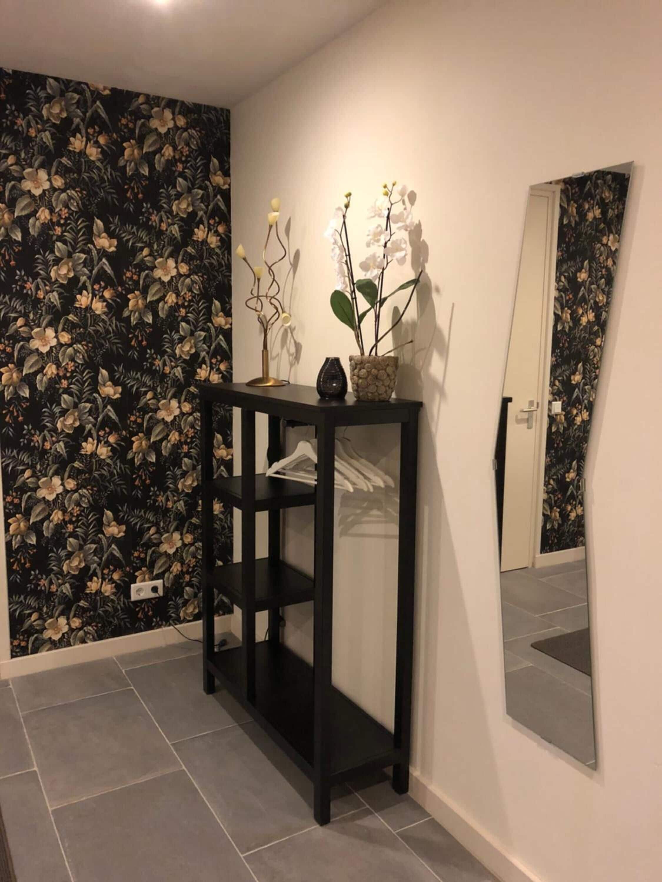 Een gang met een zwarte consoles, een spiegel en bloemenbehang.