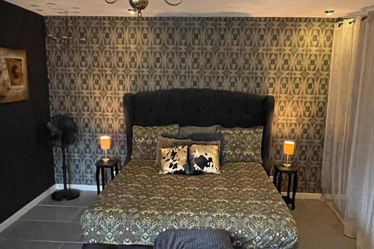 A bedroom with a large bed, a bench, patterned wallpaper, a chandelier, and two bedside lamps.
