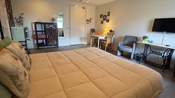 A hotel room with a large bed, a desk, a chair, a television, and a sewing machine.