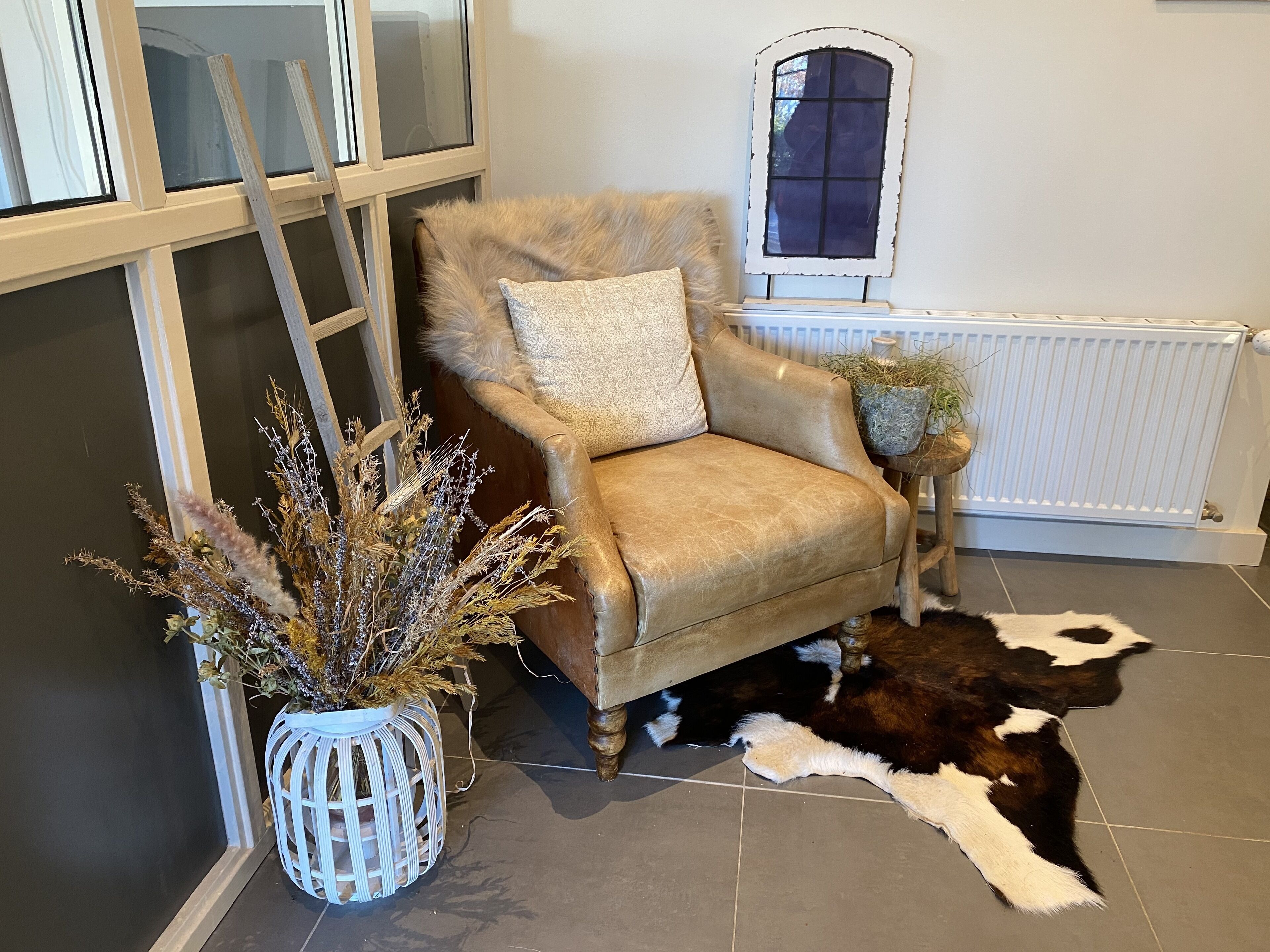 Een kamer met een leren fauteuil, een decoratieve plant en een koeienhuidkleed.
